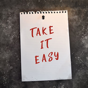 Grey background with a torn white lined spiral paper that says "Take it easy" in red block letters 