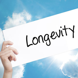 Blue sky and white clouds with sun peeking out from behind a white paper sign saying "longevity" held by a hand on the left
