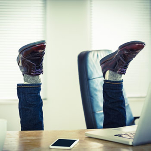 legs attached to brown loafers up in the air behind a desk with a computer in an office space