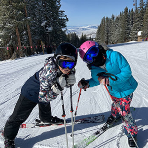 Two children in winter clothing are holding skis and posing for a picture in the snow.