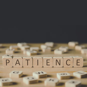 wooden scrabble letters standing up to spell "patience" with scattered letters out of focus around the word