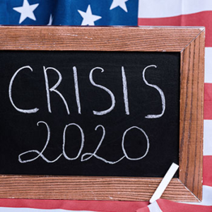 chalkboard sign saying "crisis 2020" before an American flag
